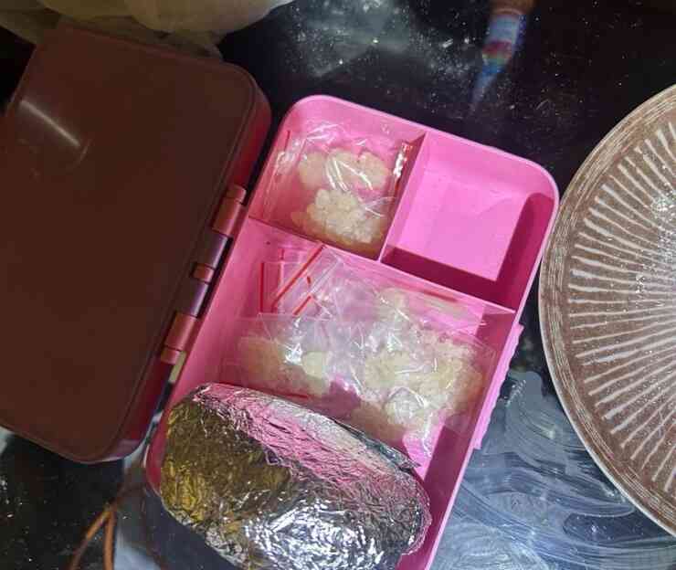 Różowy pojemnik z przegródkami z woreczkami strunowymi i zapakowaną folią paczką; na blacie leży też talerz.