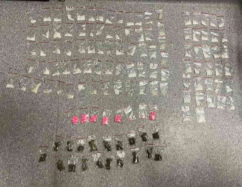 Woreczki strunowe ułożone w rzędy na podłodze oraz kilka różowych tabletek i małych pakunków.