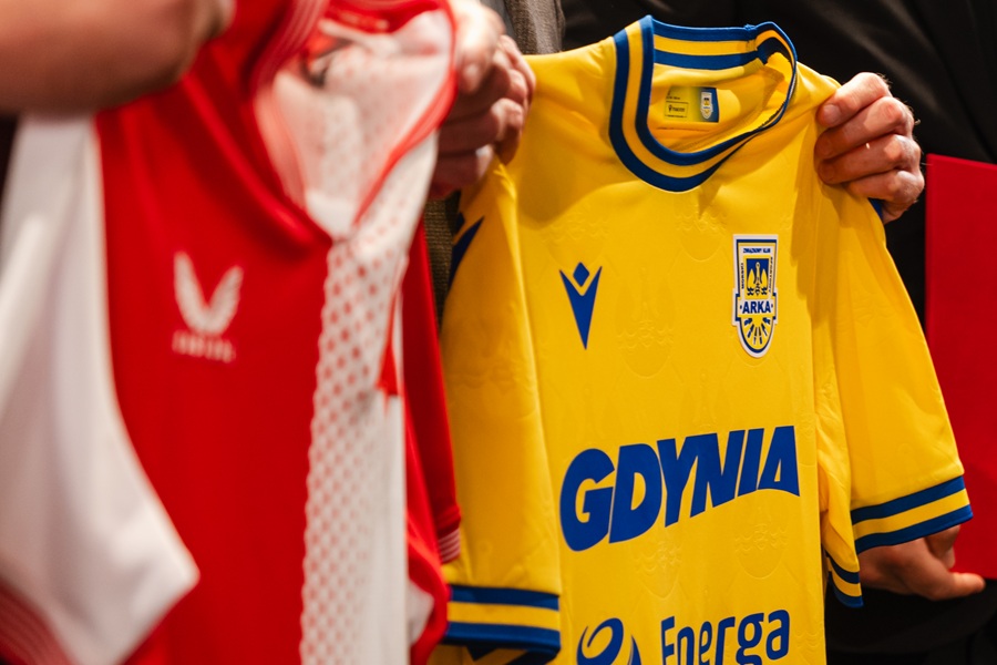 Żółta koszulka Arki Gdynia z napisem "Gdynia" trzymana obok czerwono-białej koszulki SK Slavia Praga podczas ceremonii podpisania umowy o współpracy