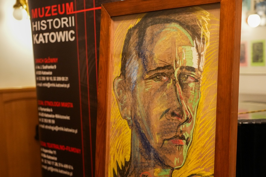 Pastelowy portret mężczyzny autorstwa Witkacego na tle rollupa Muzeum Historii Katowic. Dzieło w drewnianej ramie na tle tablicy z adresami oddziałów muzeum.