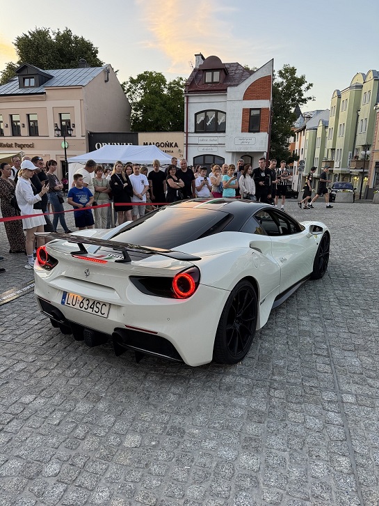 Białe Ferrari 488 GTB podczas pikniku charytatywnego Fundacji FunAndDrive Dzieciom na rynku miejskim - tłum gapiów wokół auta