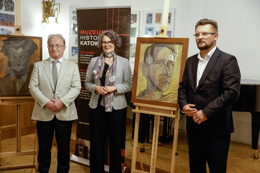 Dwie osoby i mężczyzna w okularach stoją obok pastelowego portretu Witkacego ustawionego na sztaludze w sali Muzeum Historii Katowic. W tle rollup muzeum.